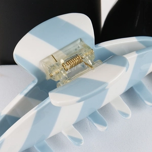 Macro shot of the sturdy gold metal spring mechanism on a blue striped claw clip