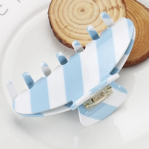 Macro shot of striped acetate hair claw clip with golden metal spring on ceramic plate
