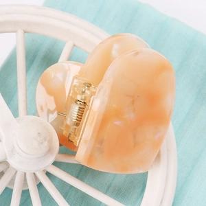 Detail einer herzförmigen Haarklammer aus Acetat in Rosa mit Marmortextur und Goldfeder