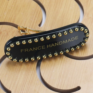 Macro detail of black acetate hair clip with gold rivets and France Handmade text