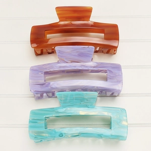 Three acetate hair claws in amber brown, lavender, and mint blue on wood background