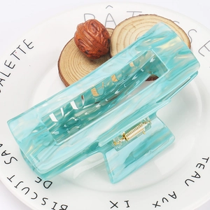 Macro detail of large acetate hair claw clip with light blue marble texture on a white plate