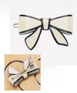Macro detail of cream acetate bow hair clip with black trim and gold metal spring fastener