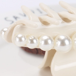 Detail of cream acetate hair claw clip featuring large pearls and glossy finish