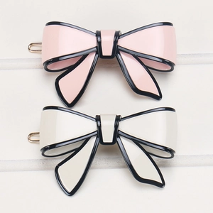 Close-up of pink and cream bow hair clips with black edges on white wood background