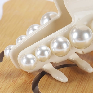 Macro shot of elegant cream acetate hair claw with glossy oversized pearls on wood base