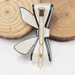 Close-up of cream acetate bow hair clip with black trim and gold metal spring closure