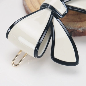 Detail of elegant cream acetate bow hair clip with black glaze edges and gold metal pin