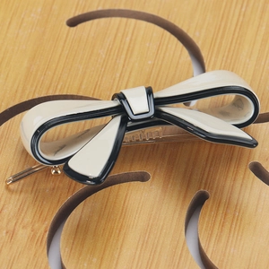 Detailed view of cream bow hair clip with black edges and gold metal alligator clip