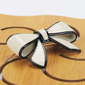 Detailed view of cream bow hair clip with black edges and gold metal clip base