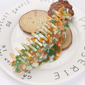 Floral acetate hair claw clip with orange and green patterns on a white ceramic plate