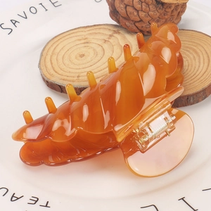 Close-up of amber acetate hair claw clip with golden spring on a ceramic plate