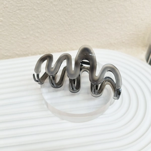 Detail of translucent gray wavy shark hair claw clip on a modern display stand
