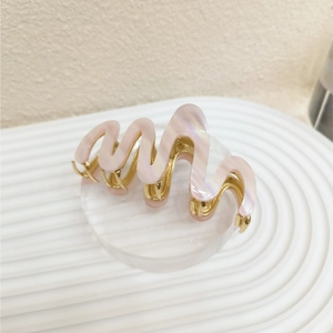 Close-up of wavy pink acetate hair claw clip with golden metal teeth on display