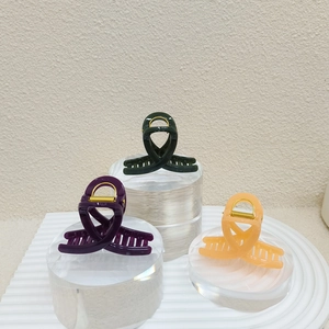 Trois pinces à cheveux en plastique brillant en violet, vert et orange sur un socle blanc