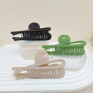 Detailed view of large PVC hair claws in black, avocado green, and beige on a white stand