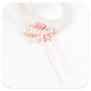 Detail of pink acrylic shark hair claw clip with elegant ribbon bow and marble texture