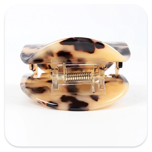 Macro shot of curved amber acetate hair claw with a premium golden metal spring