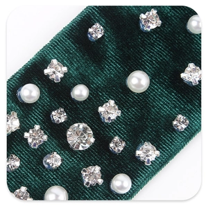 Macro shot of dark green velvet bow hair clip with embedded pearls and sparkling rhinestones