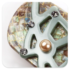 Close-up of acetic resin hair clip with rhinestones and pearl on green branch frame