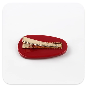 Detail of red acrylic hair clip with golden metal clip showing serrated grip structure