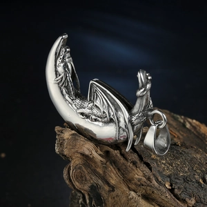 Pendentif dragon volant sur croissant de lune argenté posé sur un socle en bois