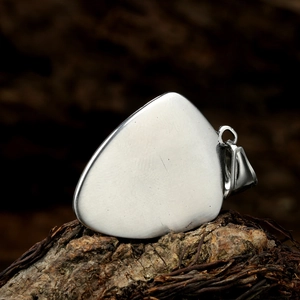 Close-up of brushed stainless steel guitar pick pendant on natural tree bark texture