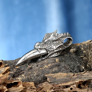 Macro shot of a punk silver dragon head pendant with bird beak on rustic wood bark