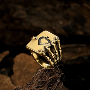 Gothic gold skeleton hand ring holding an Ace of Spades poker card on wood stand