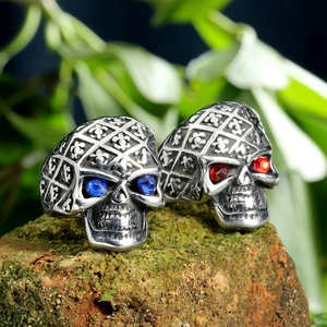 Vintage stainless steel skull rings with red and blue gemstone eyes on mossy brick