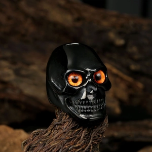 Gothic black skull ring with bright orange eyes on a rustic wood background