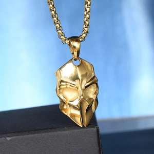 Macro view of a polished golden mask pendant on a box chain for men and women
