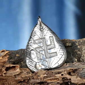 Close-up of a leaf-shaped steel pendant with engraving on a vintage wood surface