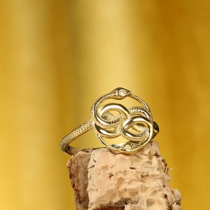 Détail macro de bague double serpent dorée aux écailles ciselées sur décor écorce