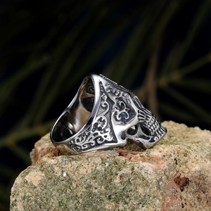 Vintage punk skull ring in stainless steel with intricate floral patterns on a rock
