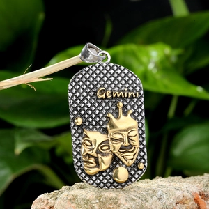 Colgante zodiaco Géminis vintage de acero con máscaras doradas sobre fondo madera