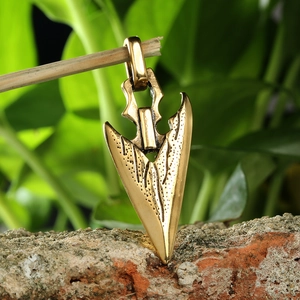 Vintage bronze arrowhead pendant in stainless steel hanging on a branch with red brick background