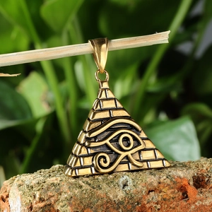 Vue détaillée du pendentif pyramide Oeil d'Horus doré suspendu à une branche naturelle
