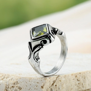 Détail macro d'une bague argentée vintage avec gemme verte carrée et reliefs ondulés