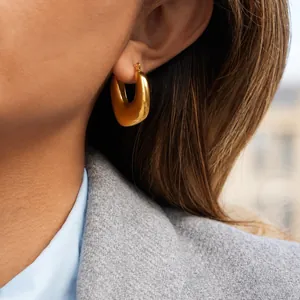 Boucles d'oreilles créoles dorées en forme de U portées par un mannequin chic