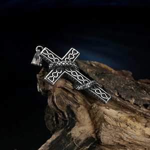 Detailed close-up of a silver gothic cross pendant with snake wrap on rustic wood