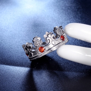 Detail eines silbernen Kronenrings mit roten Zirkonia und Kreuzmuster auf einem Display