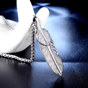 Vintage silver feather pendant necklace on artistic hand display with blue spotlight