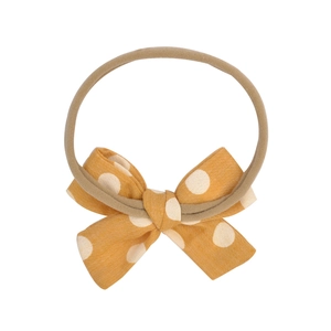 Close-up of baby headband with mustard yellow polka dot bow and soft elastic band