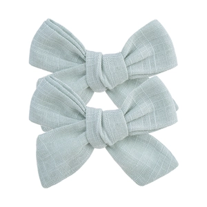 Texture détaillée de trois barrettes nœuds en lin vert menthe sur fond blanc neutre