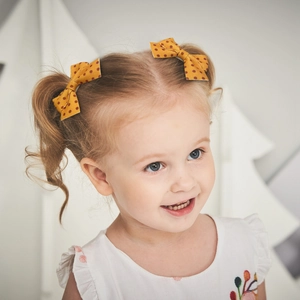 Close-up of a child wearing two yellow polka dot fabric bow hair clips for styling