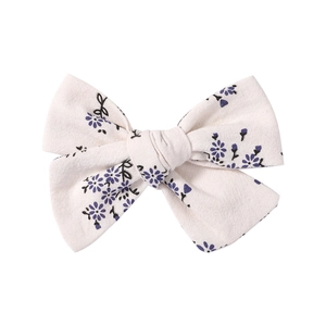 Close-up of handmade floral bow hair clip with purple flower patterns on linen fabric