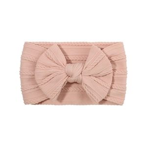 Detailed view of pink knitted baby headband with large bow and cable stitch pattern