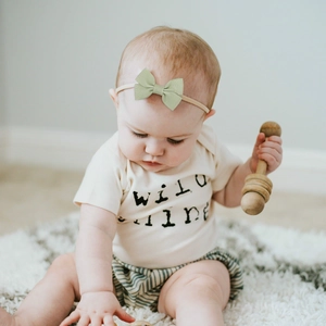 Baby girl wearing a green ribbed bow headband sitting on a soft white faux fur rug