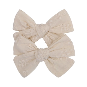 Detail of cream white embroidered cotton fabric bow hair clips in a pair for girls